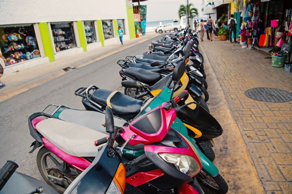 colorful scooters or motorcycles for sale or hire standing in row with wheels and lights on street road outdoor in Cozumel, Mexico, hiring transportation, traveling