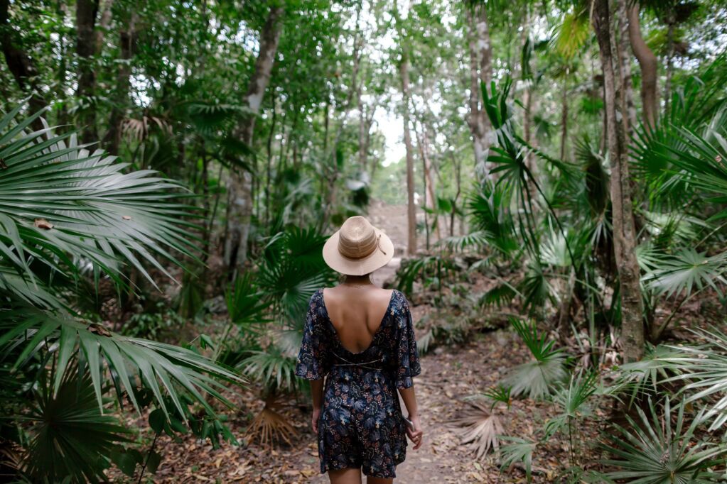 A young girl traveler in a hat stands on a path in the Mexican jungle of Sian Ka'an Nature Reserve and discover the wild and unexplored world of the jungle.
