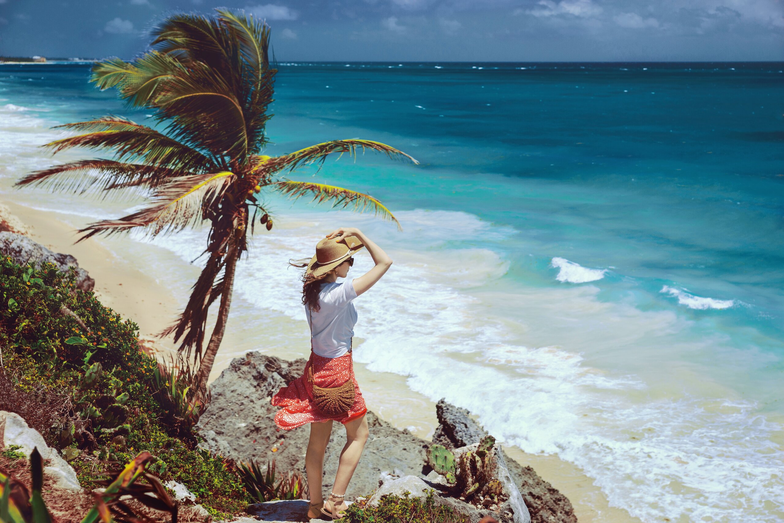 A romantic girl stands on a cliff overlooking the endless turquoise Caribbean Sea in Tulum. Paradise landscapes of Tulum on tropical coast and picturesque beach, ruins of Tulum, Mexico