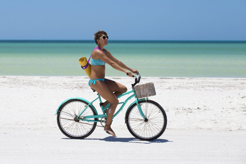Cheerful woman enjoying a day at the beach, with a bike and a yoga mat