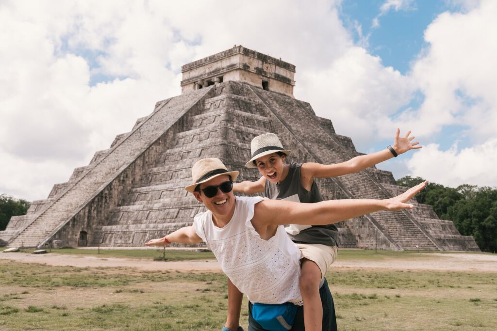 Mother and daughter happily opening their arms near the pyramid in Chichen Itza. Yucatan, Mexico