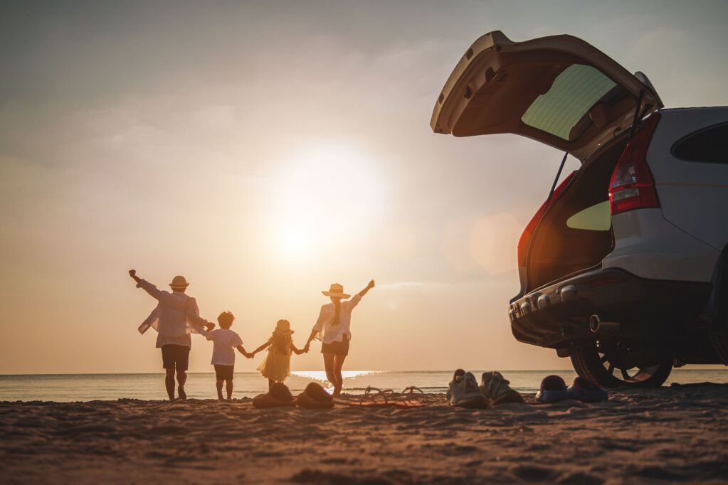 Wakacje rodzinne, Szczęśliwa rodzina działa na plaży w zachodzie słońca. Widok z tyłu szczęśliwej rodziny na tropikalnej plaży i samochód na boku. 