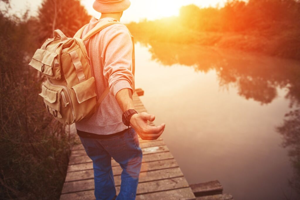 podróżnik z plecakiem chodzenie po drewnianym moście nad jeziorem w zachodzie słońca